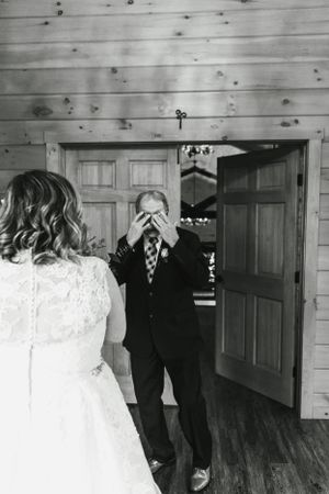 An emotional first look moment between a bride in lace and groom in a suit inside a rustic wooden room.