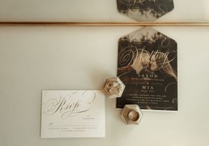 Wedding invitation suite with black and white cards and gold hexagon details on a neutral background.
