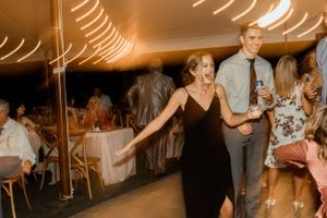 Wedding guests dancing and celebrating under a tent with warm lighting and festive atmosphere.