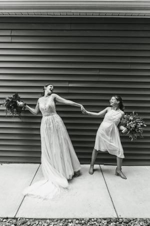 Black and white photo of two people posing creatively against siding wall.