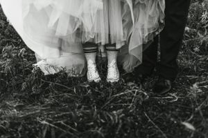 Black and white photo showing wedding dress details and boots on rustic ground.