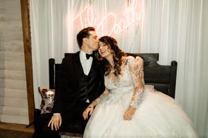 A romantic wedding scene with a couple posing under a neon sign against a white backdrop.