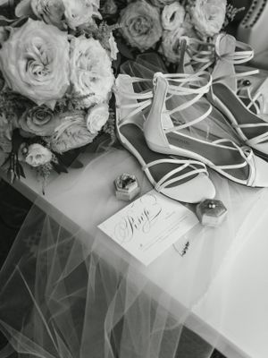 Black and white photo of bridal details including bouquet, shoes, and wedding stationery.