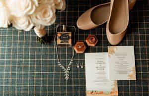 Wedding details including nude heels, jewelry, and invitation laid out on a plaid surface.
