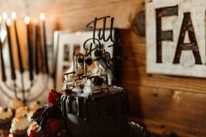 Dark gothic wedding cake with black drips and candles against rustic wooden backdrop.
