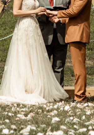 Close-up of wedding ring exchange with white dress and tan suit.