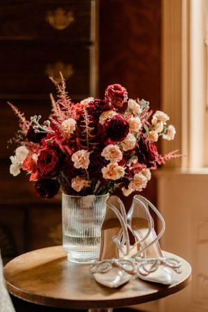 Wedding details featuring bridal shoes and romantic floral arrangement in glass vase.