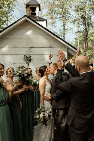Joyous wedding celebration outside white chapel with wedding party in green dresses.