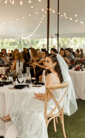 A wedding reception under a tent with string lights where guests dine at round tables with white linens.