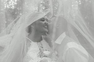 Ethereal black and white portrait showcasing a delicate lace veil against a misty forest backdrop.