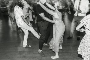 Black and white vintage photo of people swing dancing on a wooden dance floor.