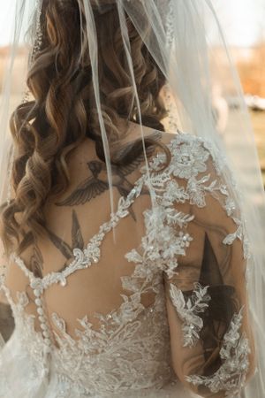 Close-up of intricate lace detailing on the back of a wedding dress with flowing curled hair.