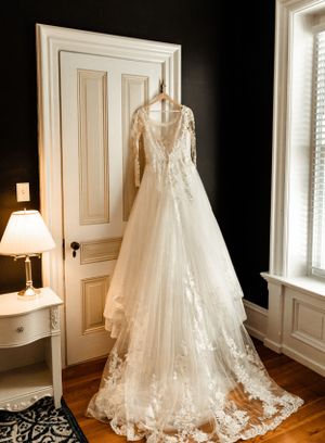 An elegant white lace wedding gown with long sleeves hanging on display in a sunlit room.
