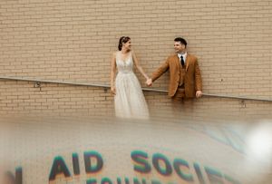Wedding couple holding hands against brick wall with graffiti reflection.