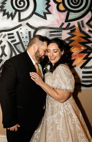 Couple sharing romantic moment against colorful graffiti wall at wedding celebration.
