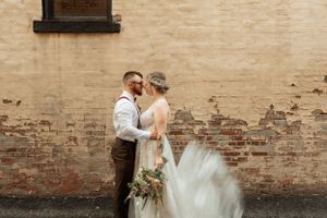 A romantic wedding portrait against a vintage brick wall with flowing dress details.