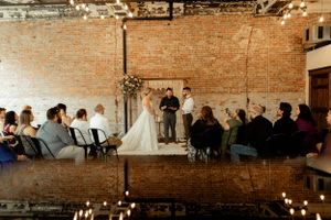 Indoor wedding ceremony setup with candles and guests seated in front of exposed brick wall.