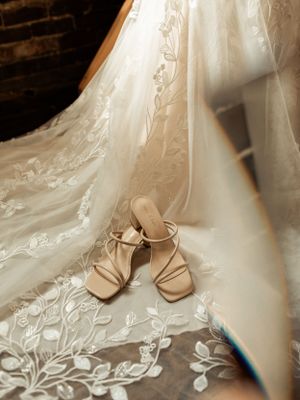 Elegant beige wedding shoes placed against the flowing train of a lace wedding gown.