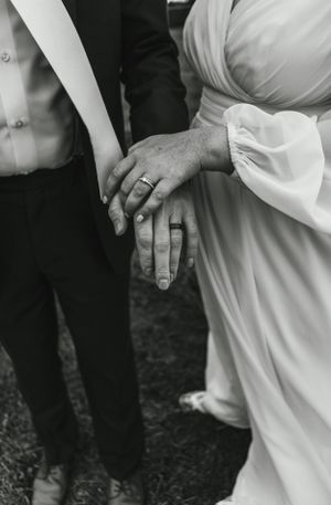 Close-up black and white photo of newly married couple's hands showing wedding rings.