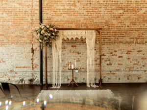 Elegant wedding altar setup with white draping and floral arrangements against a rustic brick wall.