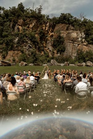 Outdoor wedding ceremony setup with dramatic cliff backdrop and white flower petals along the aisle.