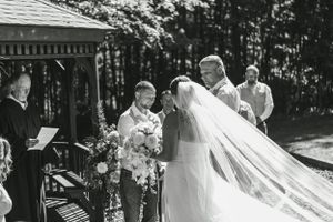 A beautiful outdoor wedding ceremony taking place at a gazebo surrounded by trees.