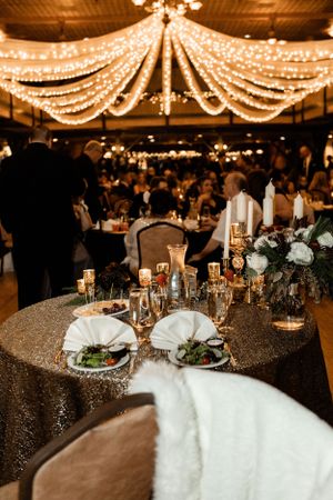 Elegant wedding reception setup with sparkling string lights overhead and a sequined tablecloth with place settings.