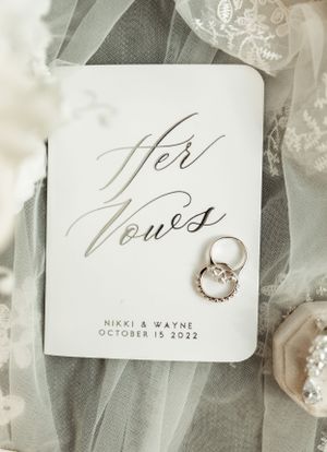 Vow book with wedding rings laid on delicate lace fabric.