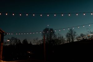 String lights illuminate a dark evening sky above silhouetted trees creating a magical outdoor ambiance.