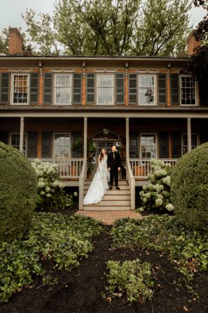 Elegant wedding couple descends stairs of a historic home with white hydrangeas lining the walkway.