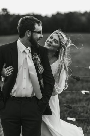A candid black and white outdoor portrait capturing a joyful wedding moment.