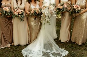 Row of bridesmaids in champagne dresses with white lace wedding gown train in foreground.