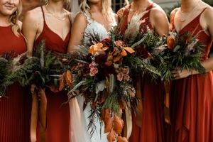 Bridesmaids in rust-colored dresses holding lush fall bouquets with greenery.