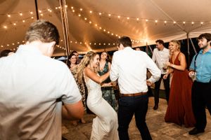 Wedding guests dancing under a tent with string lights creating a festive atmosphere.