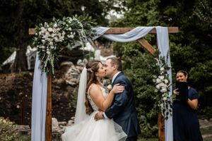 Wedding ceremony under an elegant white arch decorated with floral arrangements and draped fabric.