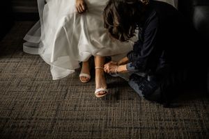 Close-up of wedding shoe being put on with white dress flowing on carpeted floor.