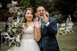 Joyful wedding celebration moment outdoors with white chairs and floral bouquet.