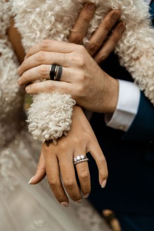 Close-up of newlyweds' hands showing wedding rings against white fabric.