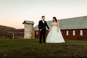 Wedding couple poses in front of a rustic barn during sunset for their countryside wedding photos.