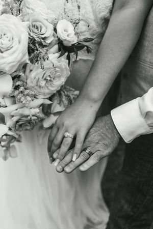 Detail shot of newlywed hands with rings alongside a classic white rose bouquet.