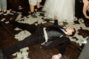 Guest lying on dance floor covered in money during wedding reception celebration.