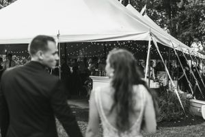 Black and white candid shot of wedding couple walking towards a decorated reception tent.