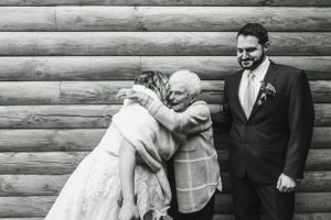 A warm embrace between wedding guests and the couple against a log cabin wall.