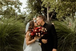 A romantic moment between newlyweds with red and pink bouquet in an outdoor garden setting.