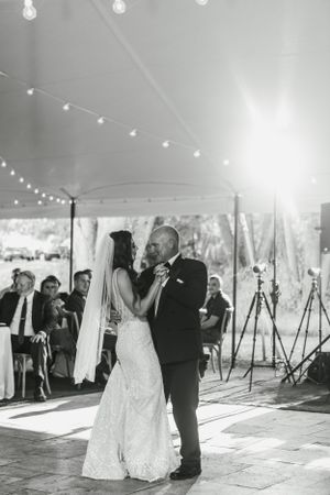 A tender first dance moment captured under a white tent with glowing string lights.