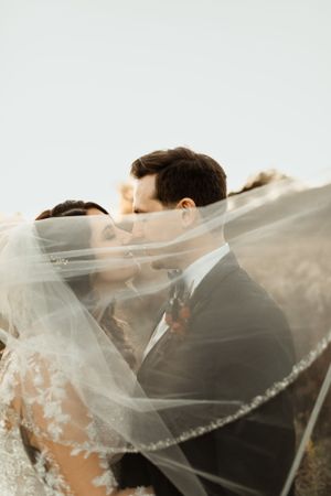 An intimate wedding moment captured through a flowing veil during an outdoor photoshoot.