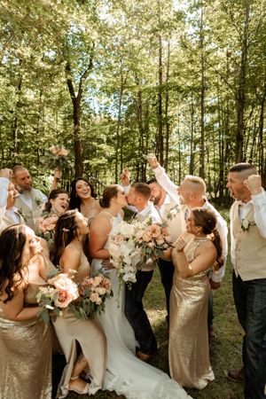 Wedding party celebrating in a sunlit forest setting with gold and champagne attire.