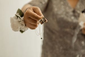 Close-up shot of hands holding delicate jewelry with white flowers in the background.