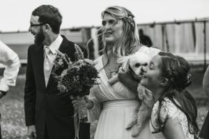Wedding party poses together with a small white dog during outdoor celebration.