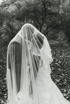 Artistic black and white photo of a bride covered in a flowing veil outdoors.